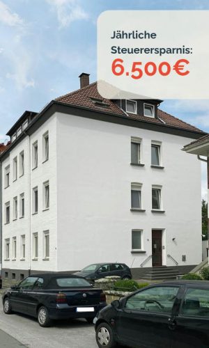 Weißes Mehrfamilienhaus mit rotem Dach.