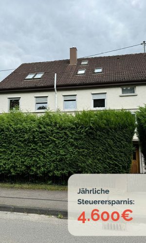 Zweistöckiges Haus mit braunem Dach, Hecke im Vordergrund.